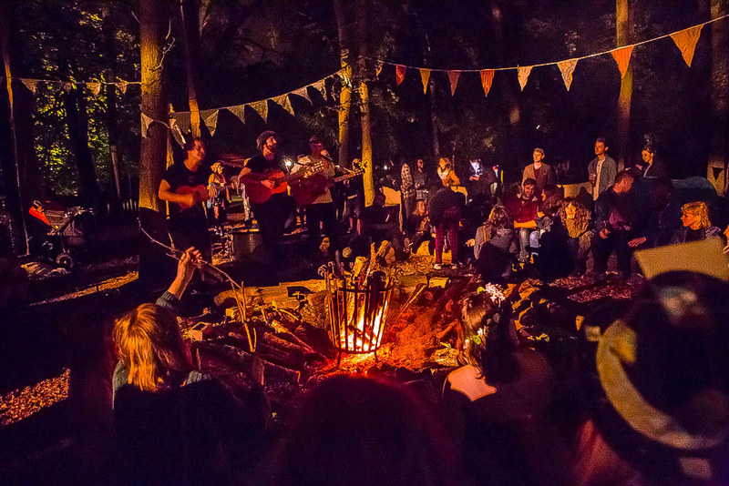 A band plays to an audience of families sat round a campfire in a woodland