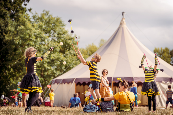 Two children dressed as bees play outside a large circus tent at Just So Festival