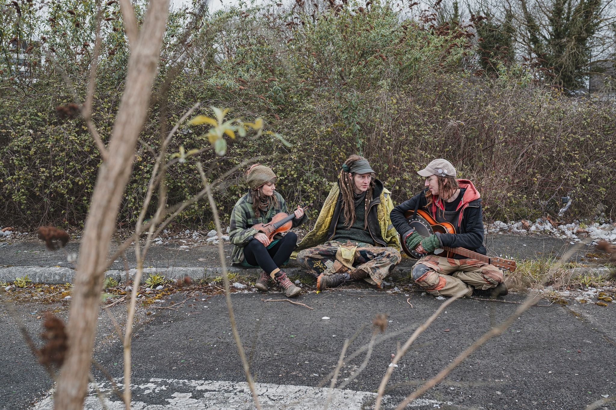 Three people from the Ragged Storytelling Collective sat on the ground with instruments